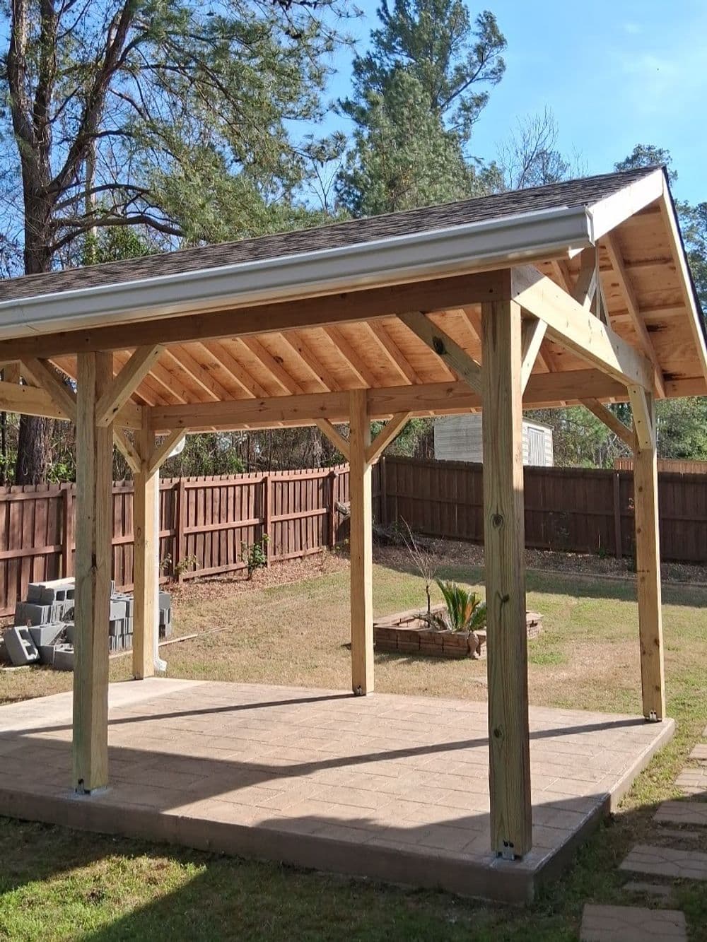 Wooden backyard gazebo with a sloped roof, surrounded by grass and greenery.