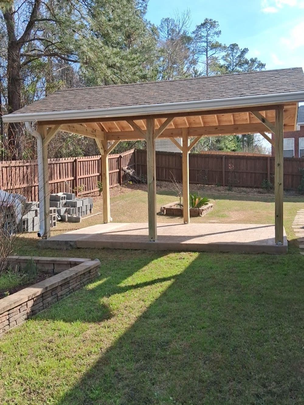 Wooden outdoor pavilion in a backyard with a grassy area and stone landscaping.