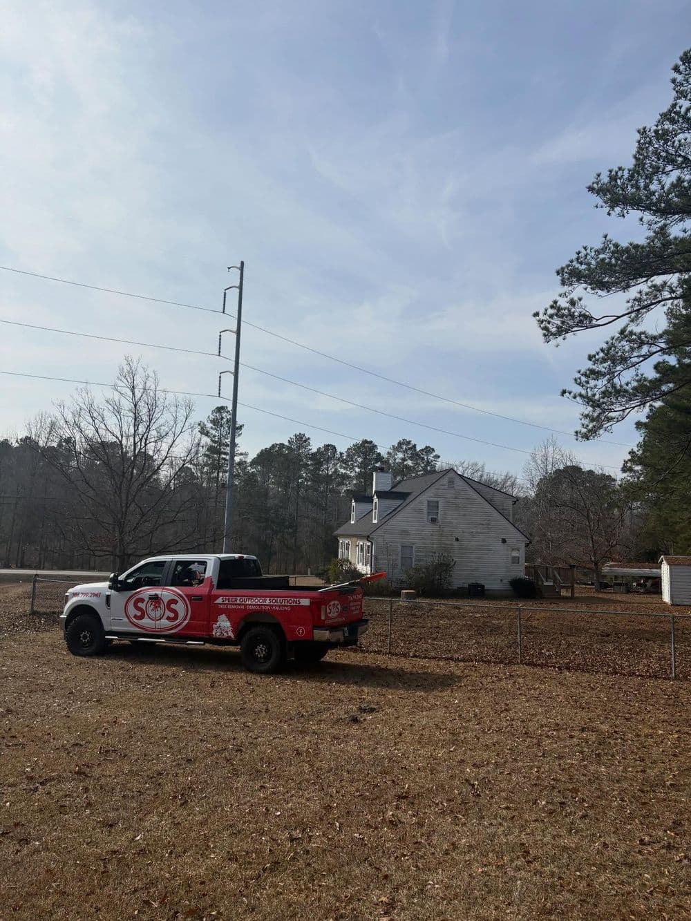 SOS service truck parked near a house surrounded by trees and power lines on a clear day.