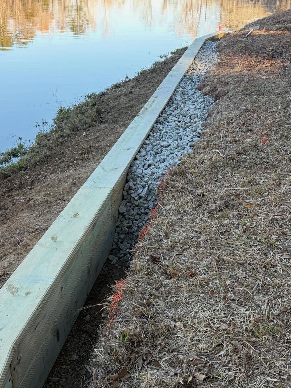 Lakeside gravel drainage solution with wooden edging to prevent erosion.