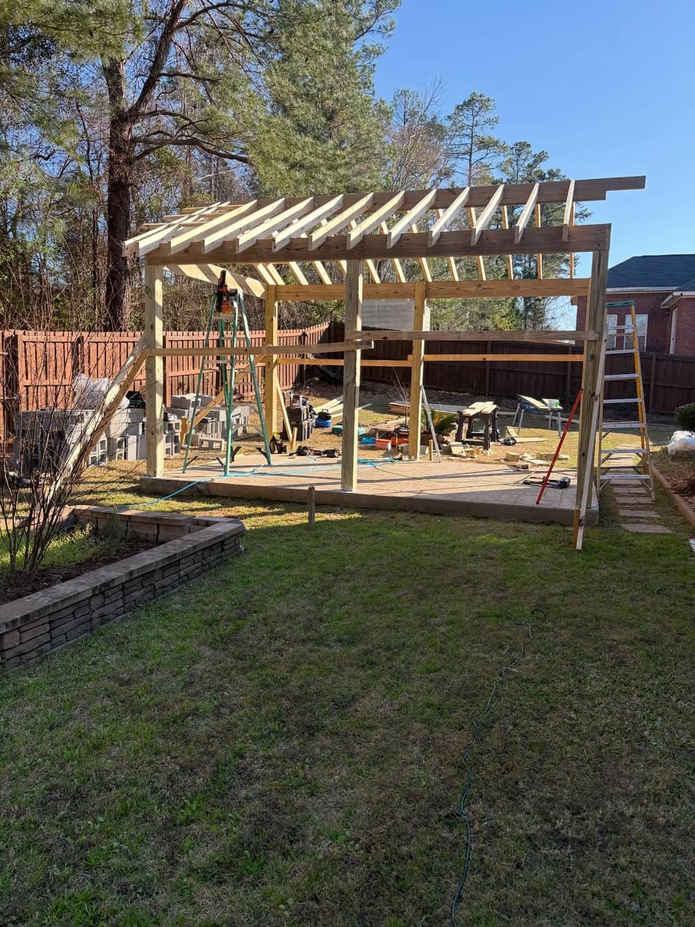 Construction of a wooden structure in a backyard, showing framing and tools.