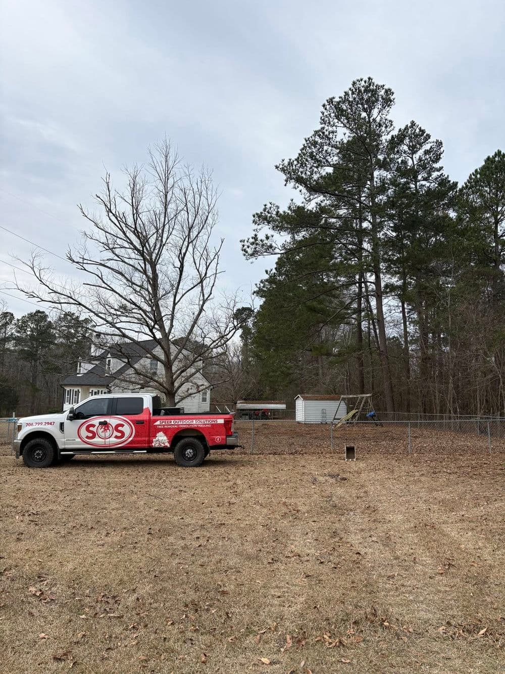 Red truck with SOS logo parked in a yard with a house, trees, and swing set in the background.